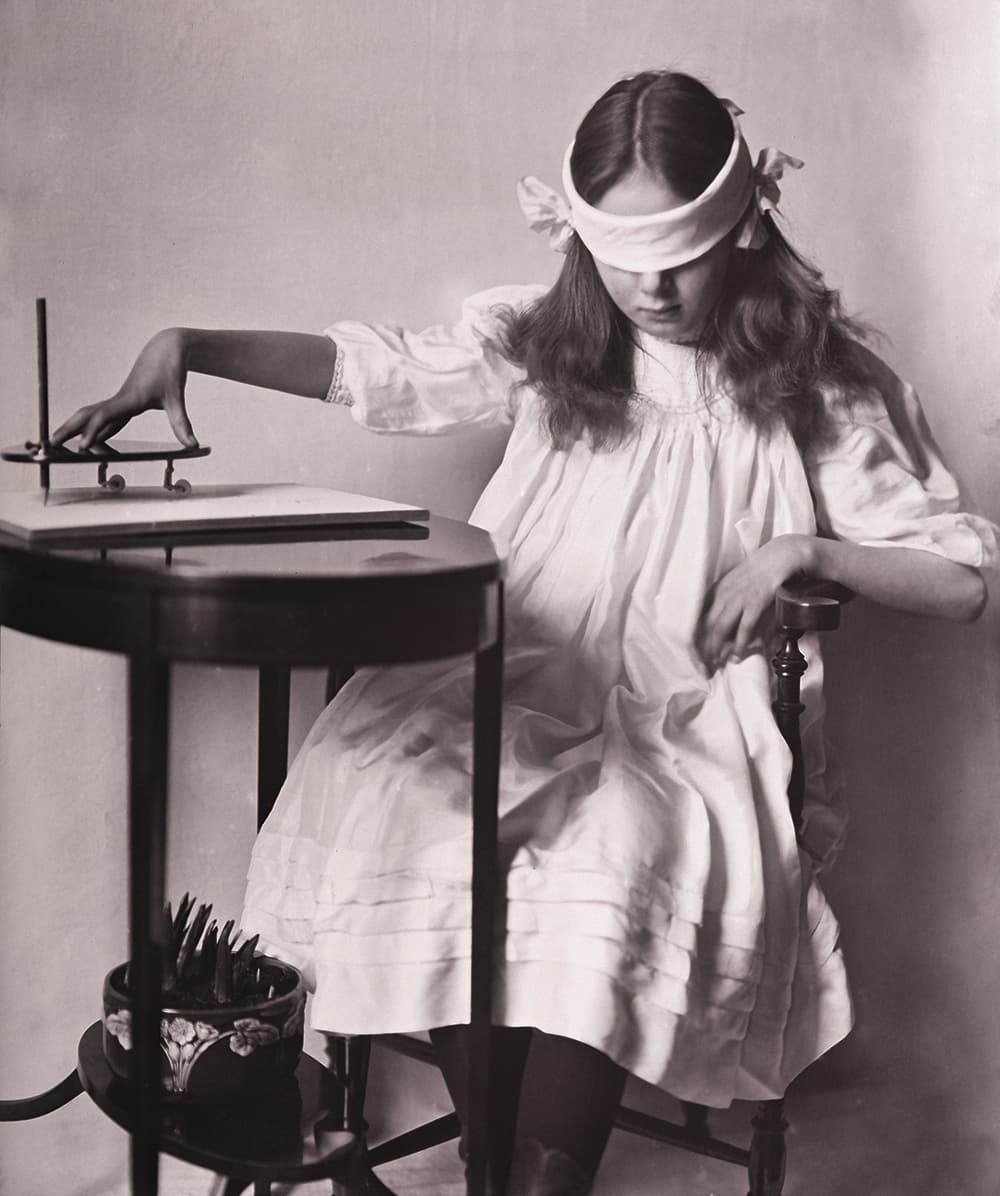 A blindfolded woman guiding a planchette across paper